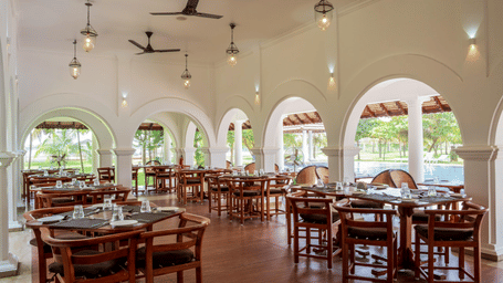 An indoor restaurant dining room featuring dark wooden tables and chairs set under white arched walls and columns | Le Pondy