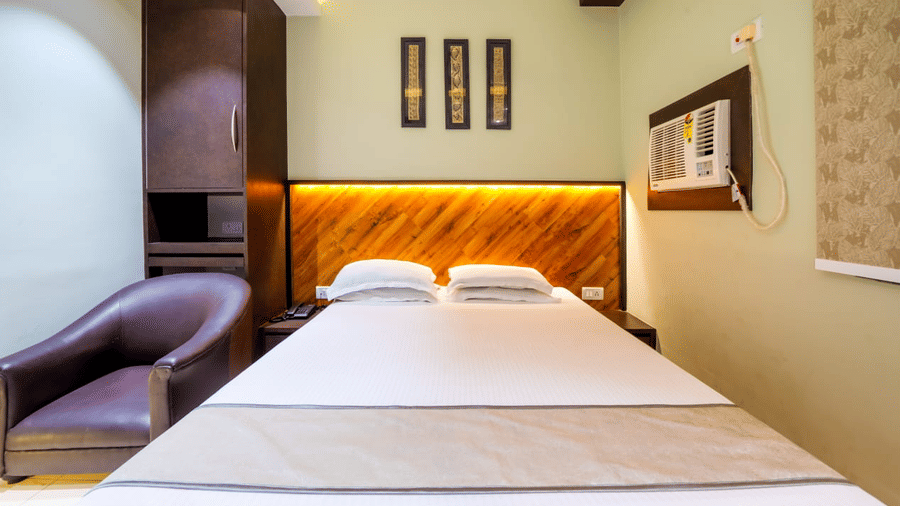 Room with a double bed, wooden furniture, window A/C, and framed pictures on the wall – Hotel Dolphin Puri