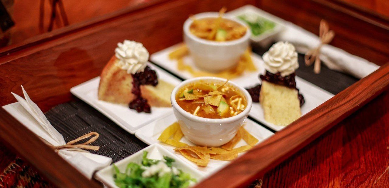A tray of appetizers or small dishes, including dips, vegetables, and other snacks, arranged on a wooden table.