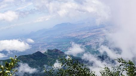 A breathtaking view of mist-covered mountains with lush greenery, clouds rolling through the peaks, and a distant valley below.