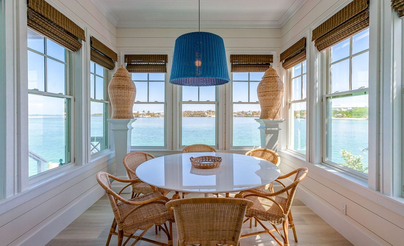 Dining area with a round table, wicker chairs, and ocean views through large windows | Abaco Inn