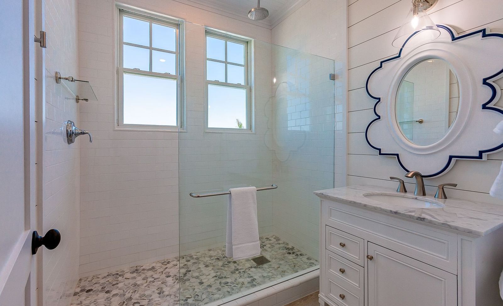 Bathroom with a glass shower enclosure, white vanity, and a decorative mirror with blue trim | Abaco Inn