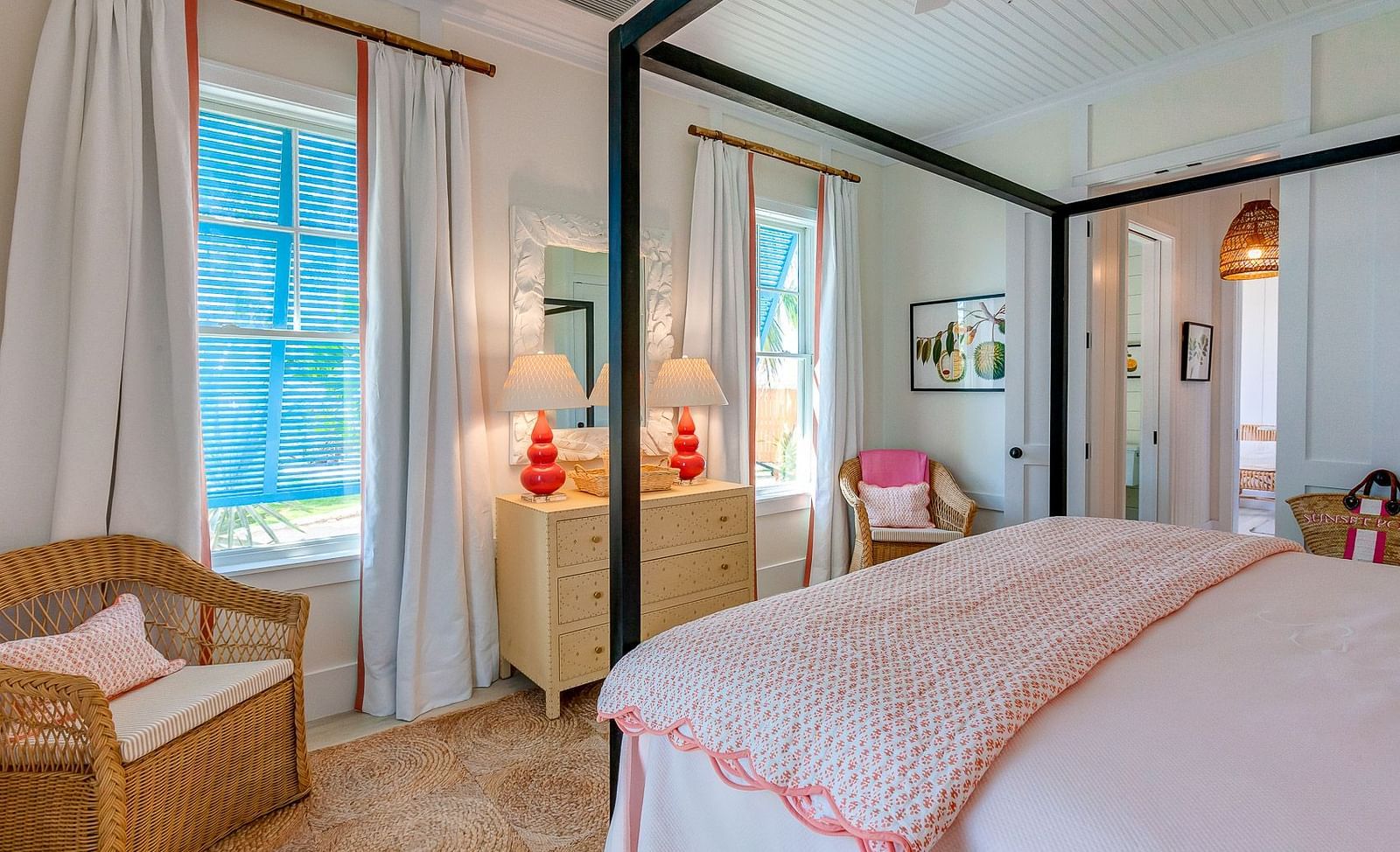 Bedroom with a pink-trimmed bed, wicker chair, red pendant lights, and large windows with curtains | Abaco Inn