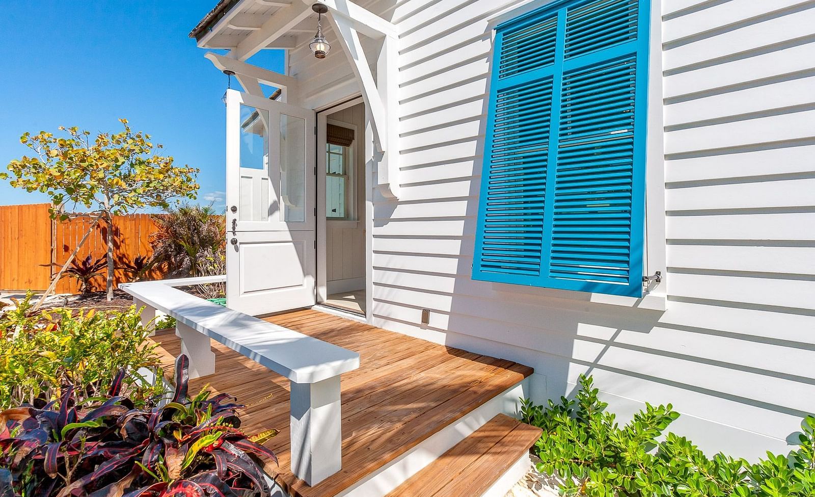 Side patio with a wooden bench, blue shutters, and lush greenery | Abaco Inn