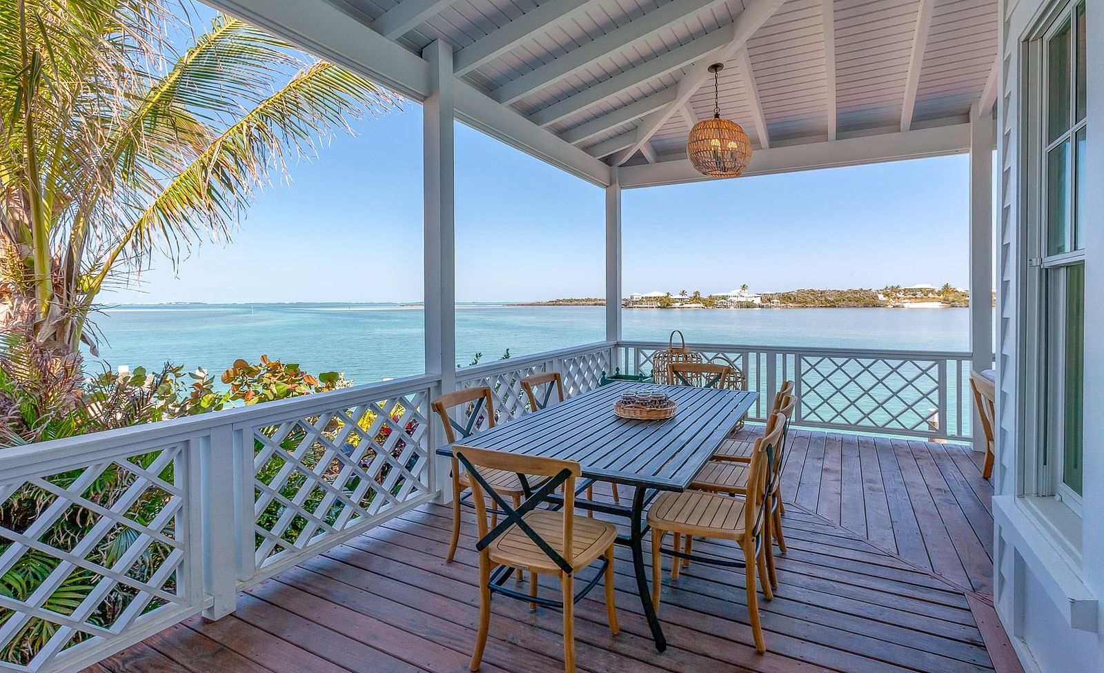 Outdoor dining area on a wooden deck with white railings, overlooking the blue sea and tropical surroundings | Abaco Inn