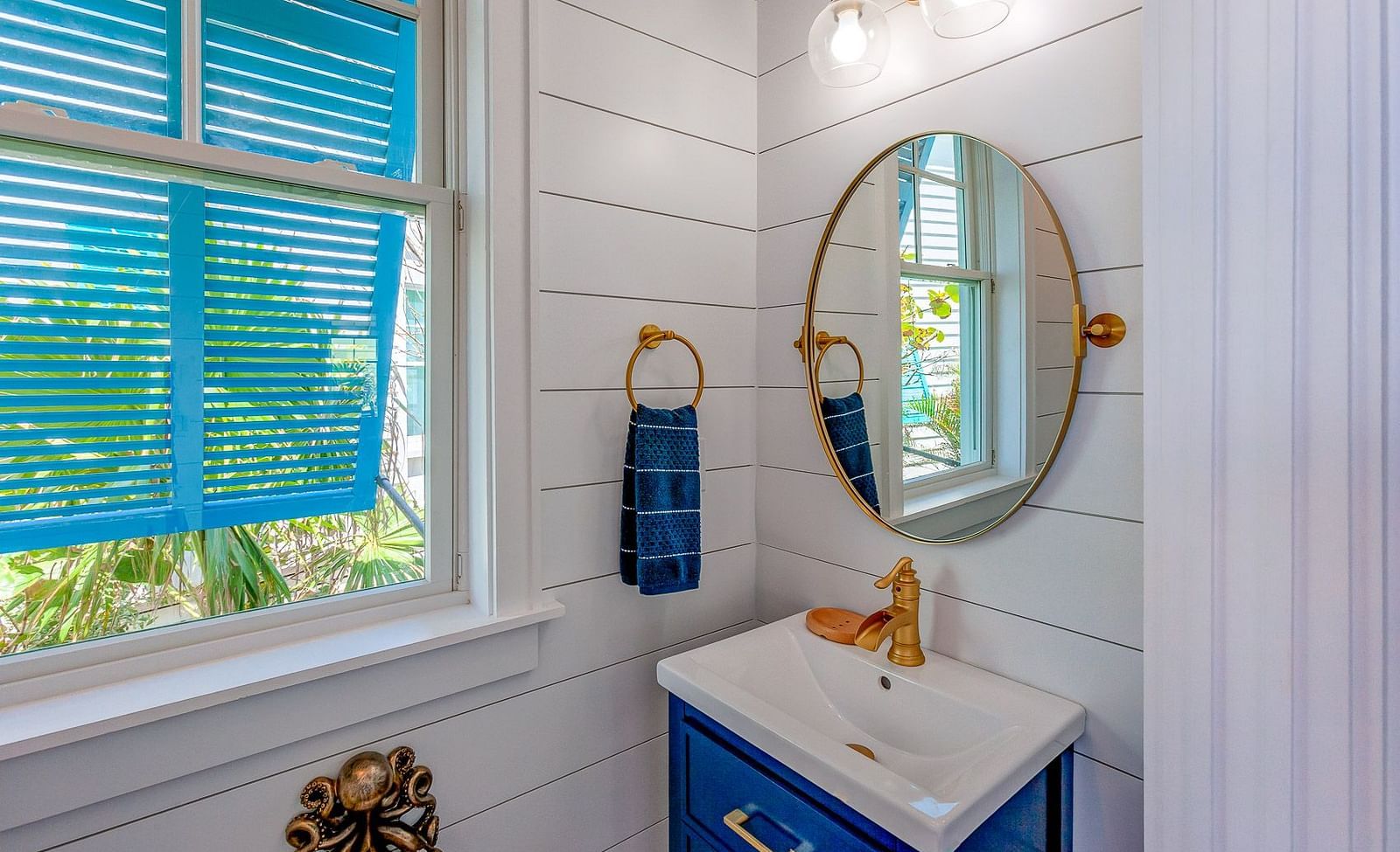 Bathroom with a white vanity, round mirror, and blue shuttered window | Abaco Inn