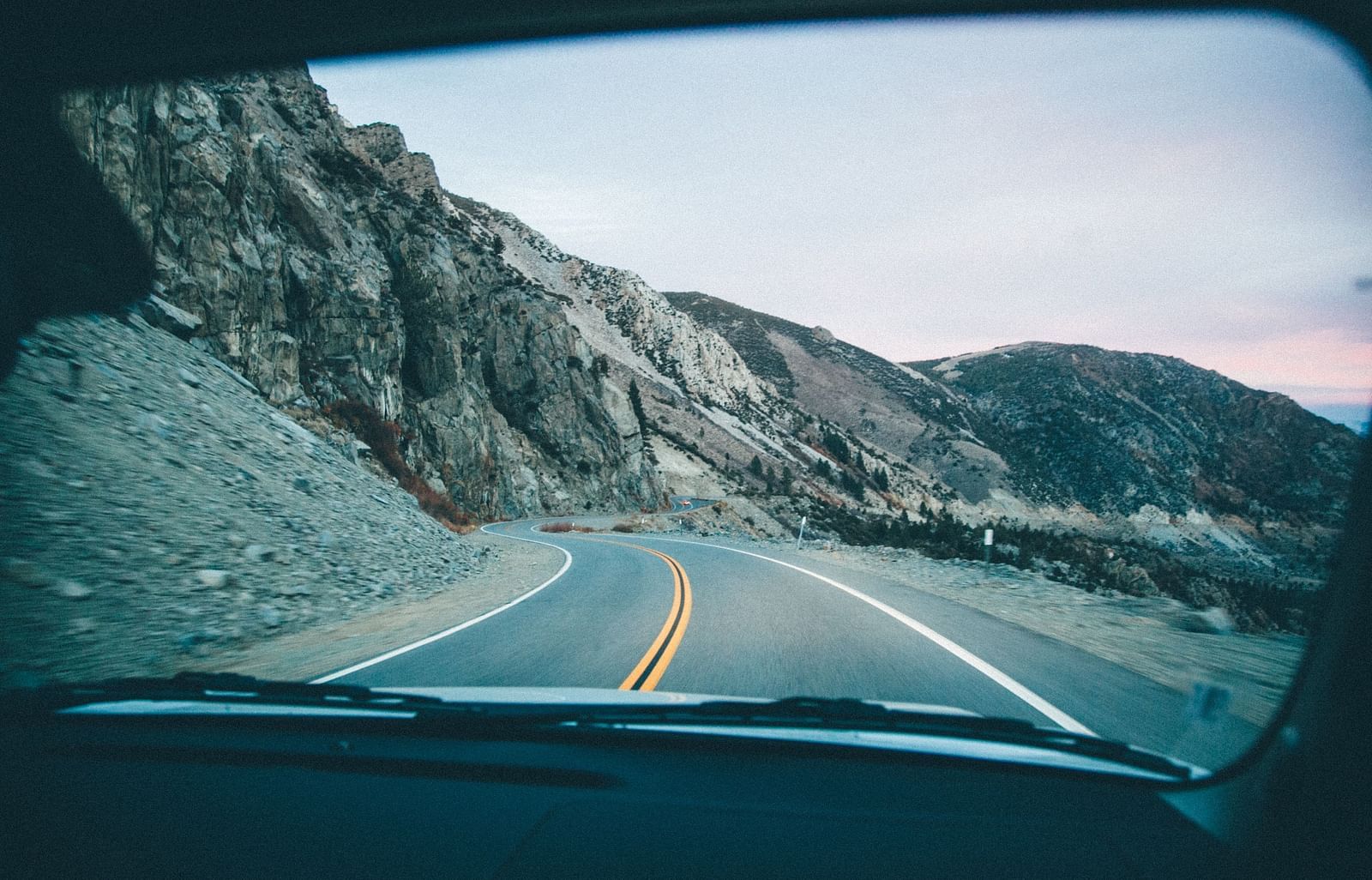 an image captured inside of a vehicle, featuring the road ahead surrounded with the mountain range followed.