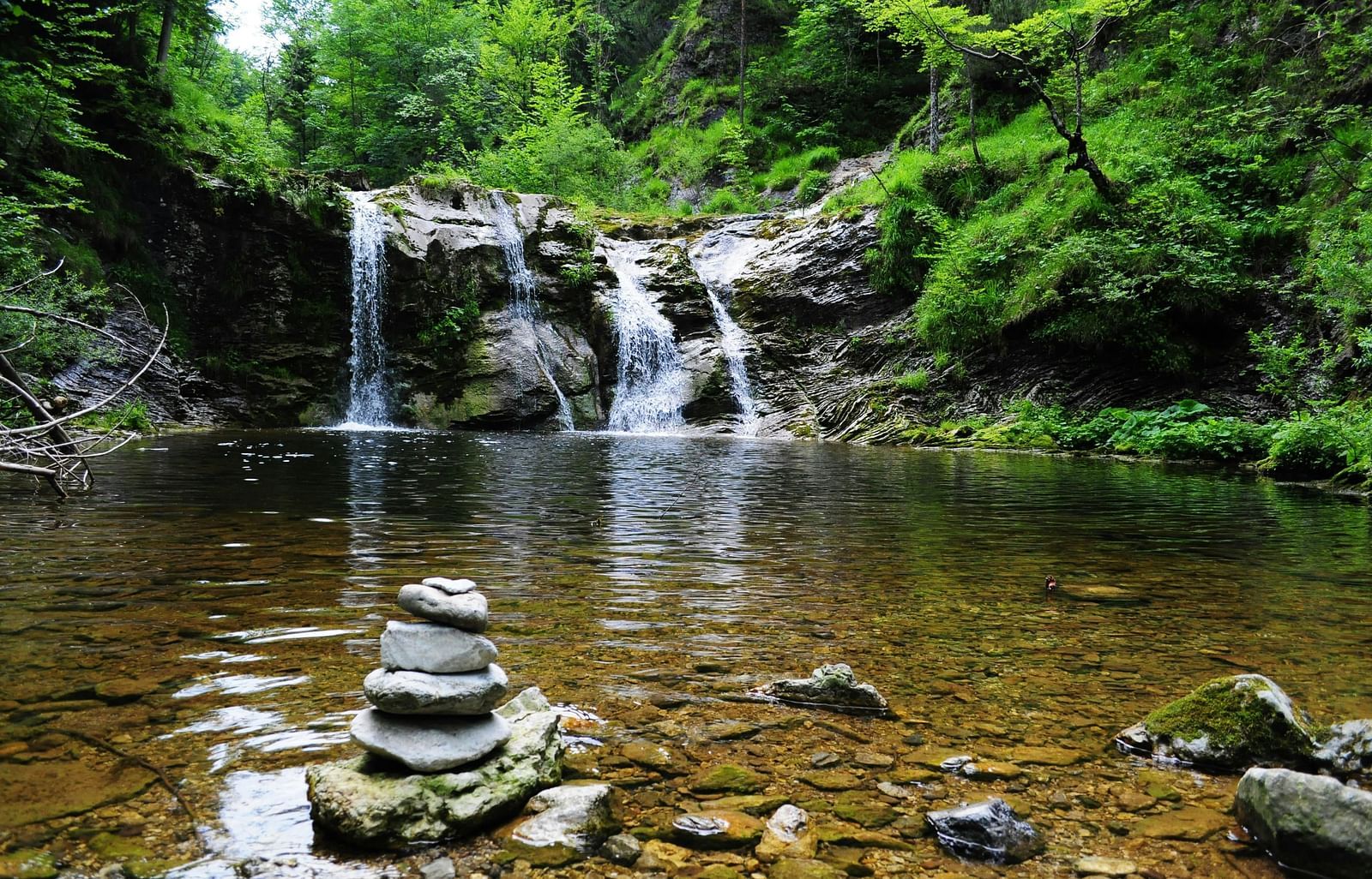 A image with tranquil waterfall cascading into a pond, surrounded by stacked stones.