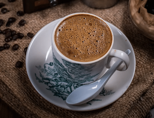 A cup of a drink on a saucer with a spoon.