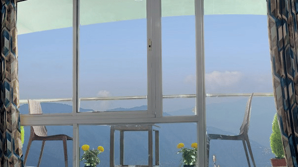 Balcony with two chairs, one table with small plants placed near the chairs and a big glass window at A room with double bed, Framed art work on the wall, TV, Wardrobe, Dustbin, Table and desk with two water bottles on the top at Central Heritage Resort an