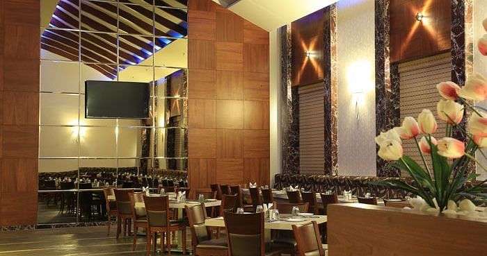 A grand dining area with high ceilings, wooden panel walls, and soft lighting for an upscale experience. - Dhanalakshmi Srinivasan Hotels, Perambalur