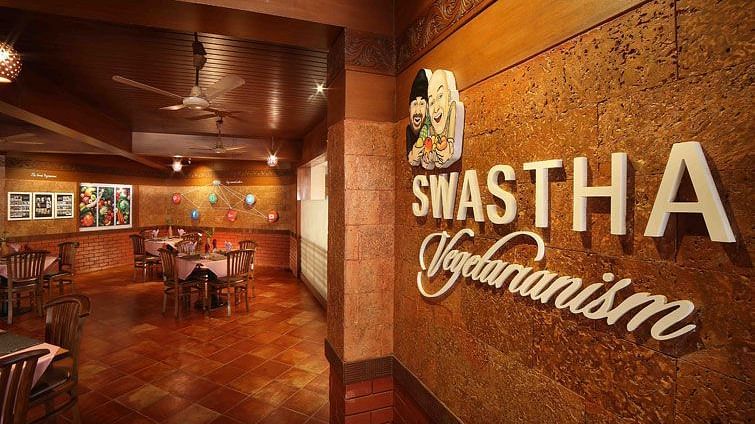 Entrance to Swastha Vegetarianism restaurant featuring a warmly lit interior, wooden furniture, and decorative walls with the restaurant's name displayed at Uday Samudra Leisure Beach Hotel, Kovalam