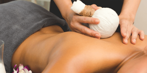 Poultice massage being performed on the spine of a person lying on their stomach