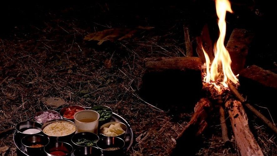 Jungle Cooking - Sajan - a thali meal of 10 items placed on the grass beside a camp fire.