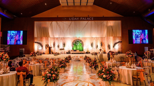 Interiors of Uday Palace Convention Centre with floral and table arrangements and a large stage decorated with lights and flowers with a fancy divan