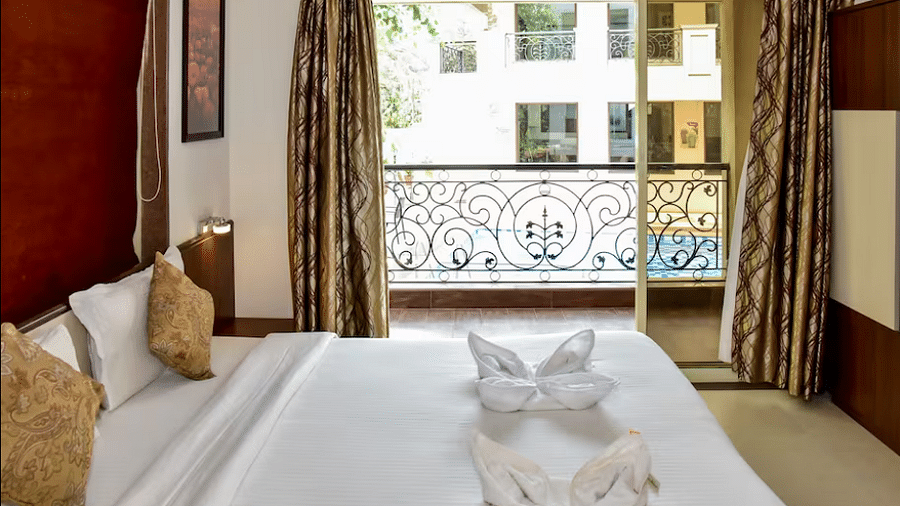 Cosy bedroom with golden cushions, towel swan decor, and a French balcony overlooking greenery at La Vida Studio Inn.
