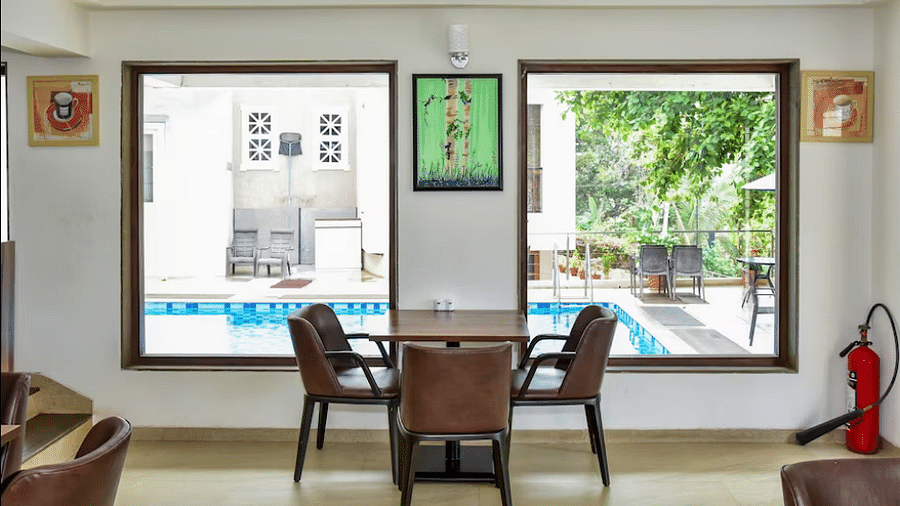 Dining space with wooden table and chairs near poolside windows, filled with natural light at La Vida Studio Inn.