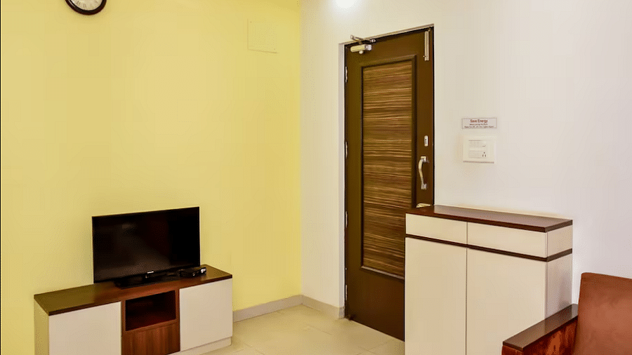 Compact entertainment area with wall-mounted TV, light yellow accent wall, and a wooden sideboard at La Vida Studio Inn.