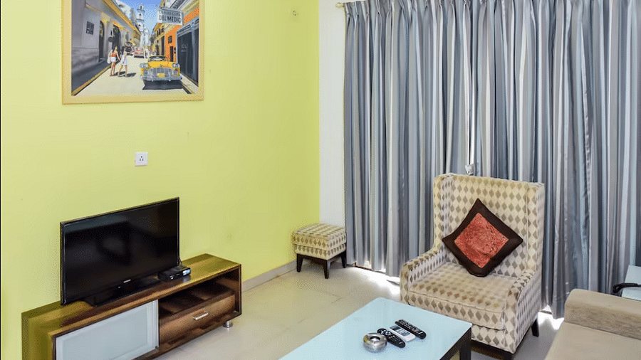 A spacious room with a television, armchair, and a small table at La Vida Studio Inn Goa.