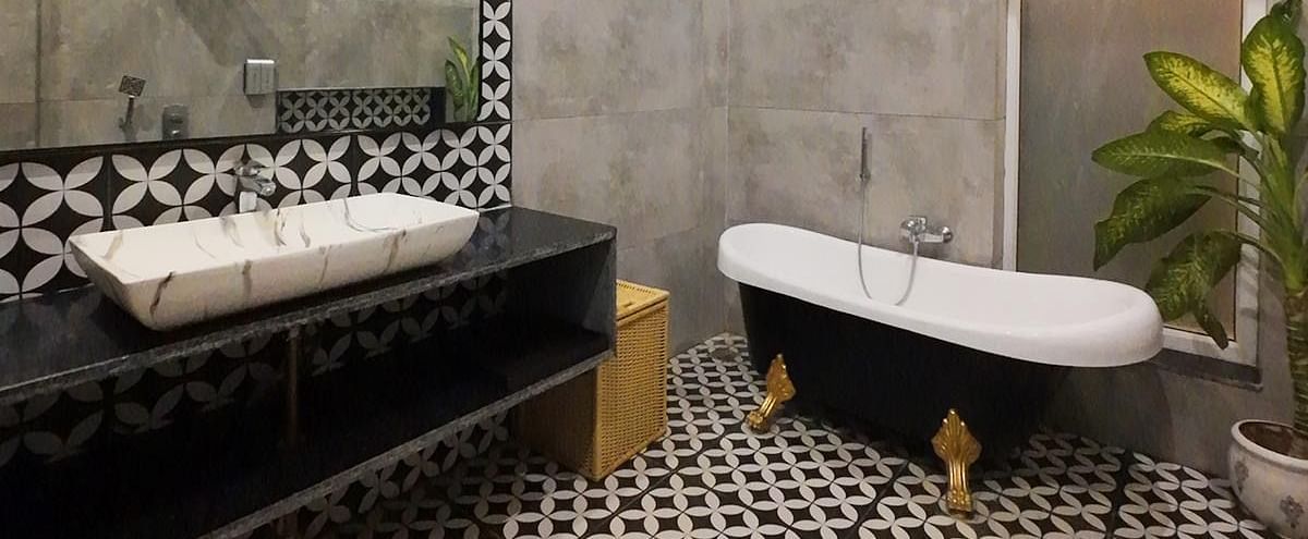 A bathroom at Tisya Farms, Gurgaon with a bathtub, two sinks, patterned flooring, and a concrete wall with a plant in the corner.