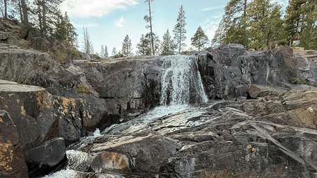 A thin stream of water flowing over the rocky cliffs with pine tree vegetation at the Rancheria Falls.
