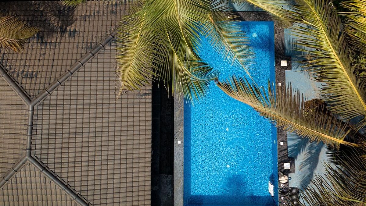 A view from above, looking down at a bright blue swimming pool surrounded by greenery and the side of Kssemya.