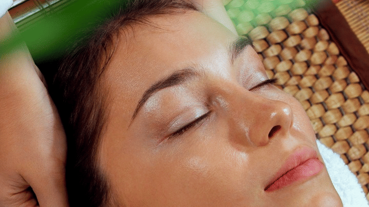 A woman lying down while receiving a head massage at Rhythm Lonavala, with a therapist applying oil to her forehead as part of a relaxation treatment captured in the image