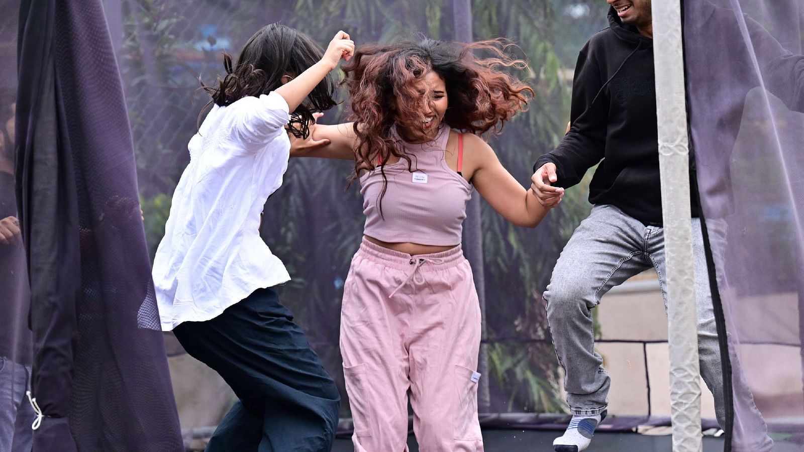 A close up shot of a group of people jumping on a trampoline with tree cover in the background.