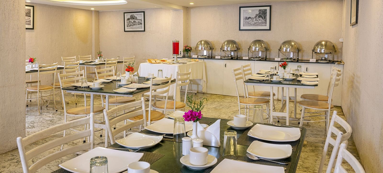 Modern buffet setup in a bright restaurant with white chairs and tables | Mango HIll Central, Ooty