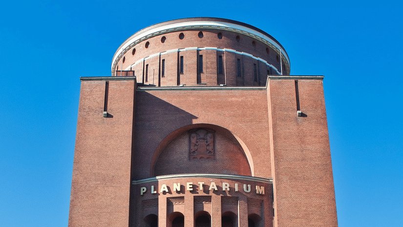 A facade view of a Planetarium Building made of red bricks with the blue sky in the background.