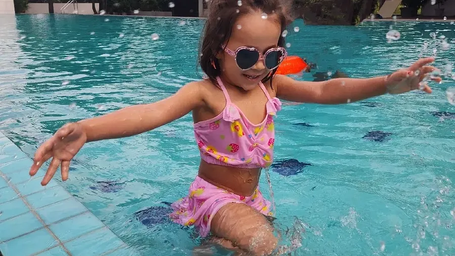 A girl in a swimming costume standing in a pool with arms raised at Karma Chalets.