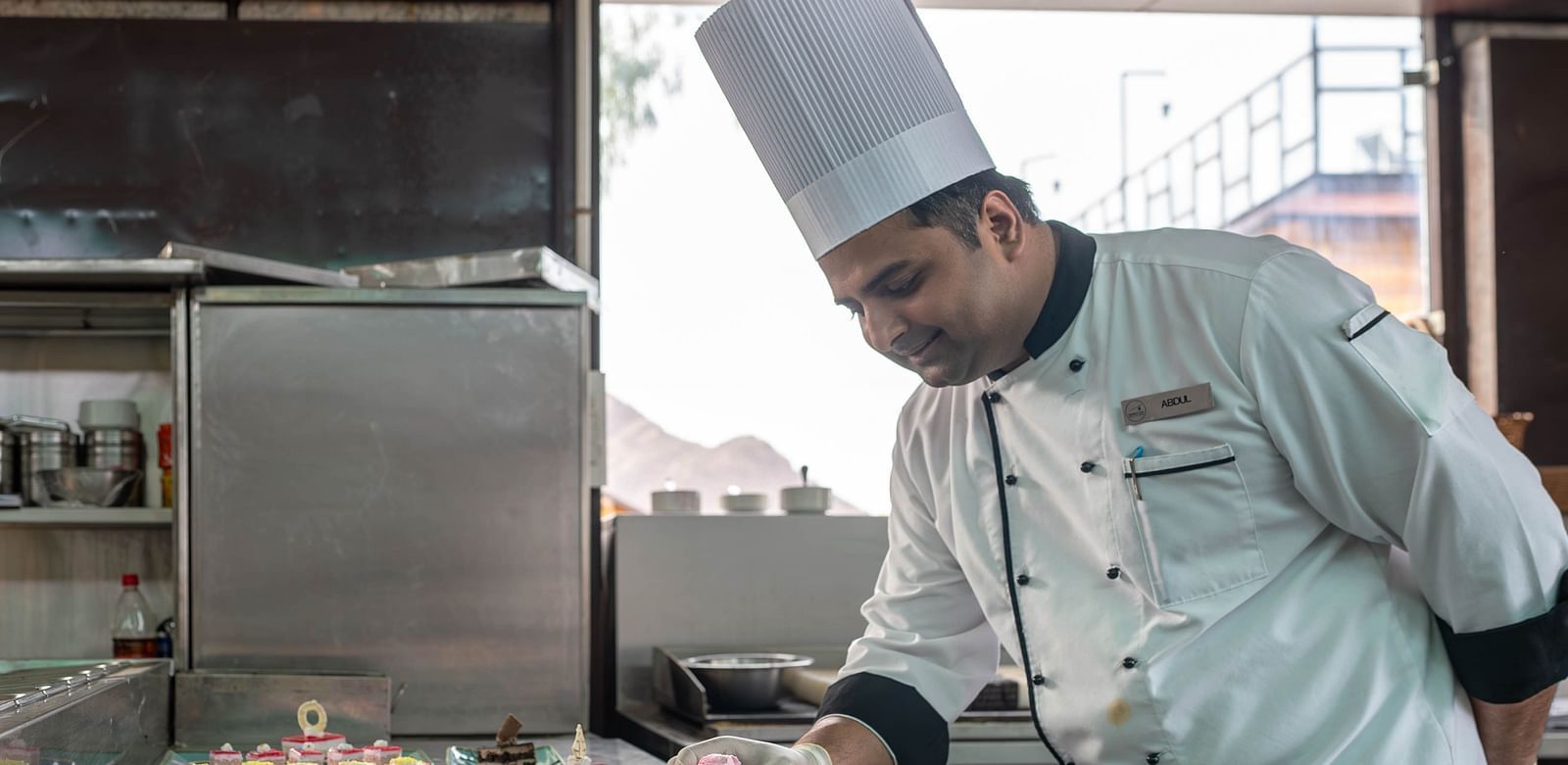 A chef in a white uniform and a tall chef's hat working in a kitchen.