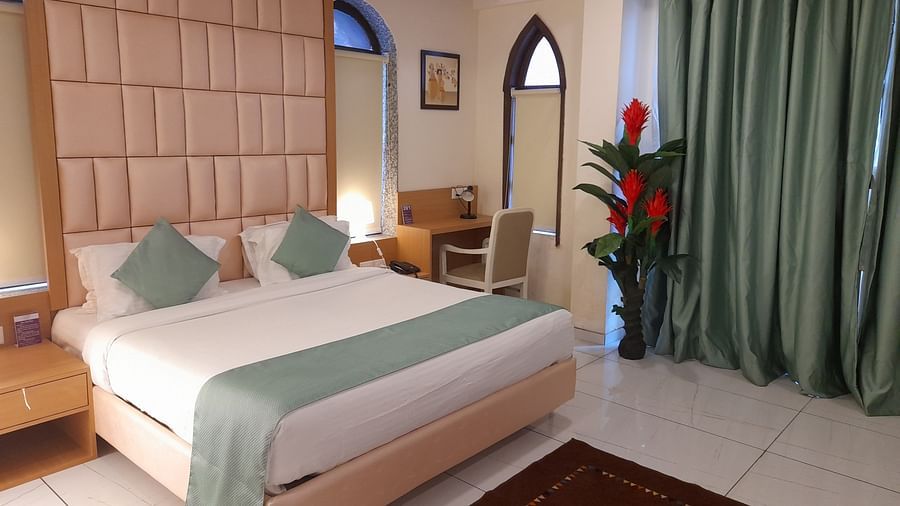 An elegant bedroom with a large bed, work desk & chair, and green curtains - VITS ExcellenSea, Dapoli