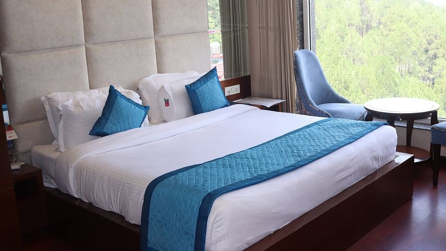 Side view of Deluxe room with plush bed and bedside tables, seating area with coffee table - Mastiff Hotel, Dalhousie