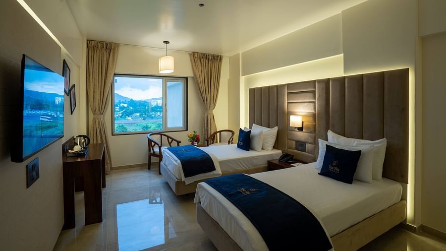 Side view of the Deluxe Twin with twin beds TV set seating area with windows and curtains - Mastiff Grand - The Sia Palace Suites Banquets Khopoli