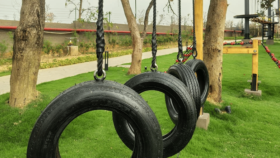 An outdoor activity area featuring 3 black tyres hanging from ropes on a wooden frame at Hotel Sonar Bangla, Ajodhya Hills.