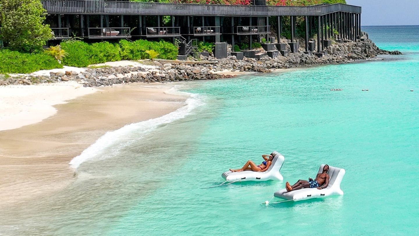 A vibrant beach scene featuring turquoise water, white sand, and a small boat near a cliffside resort.
