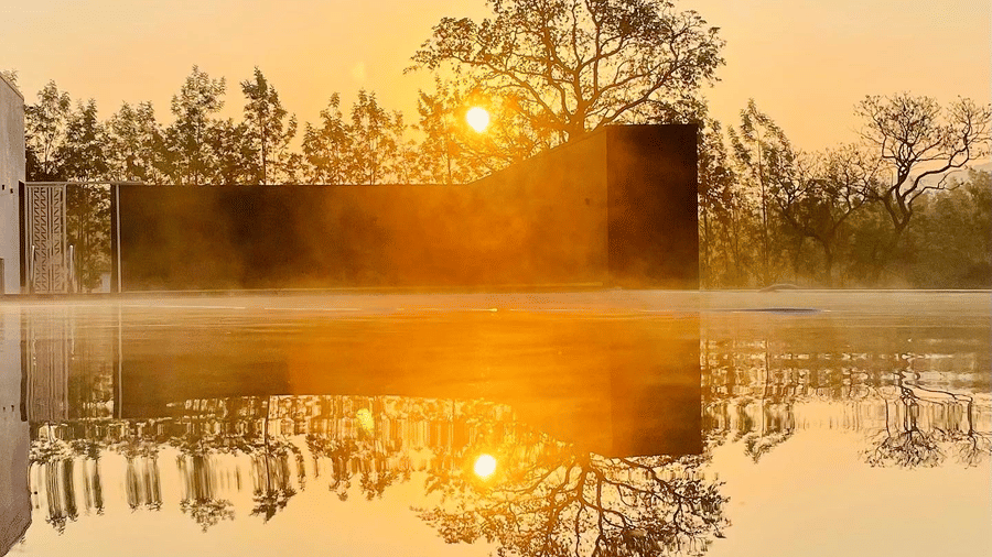 Bright sun rising over distant trees, reflecting perfectly on a still body of water at Bindiga Peak Resort.