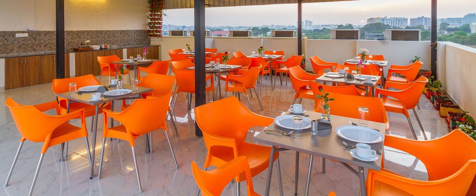 An open-air rooftop dining area with orange chairs and numerous tables at Sanctum Suites Whitefield, Bangalore.