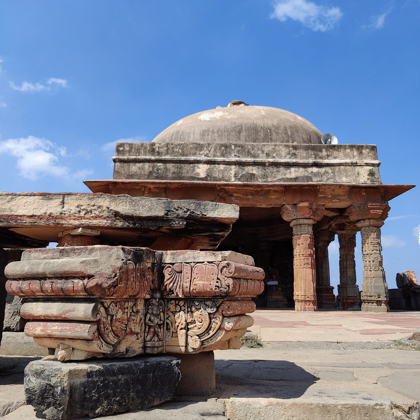 Ancient, weathered stone ruins including a dome and pillars stand beneath a clear, vibrant blue sky.