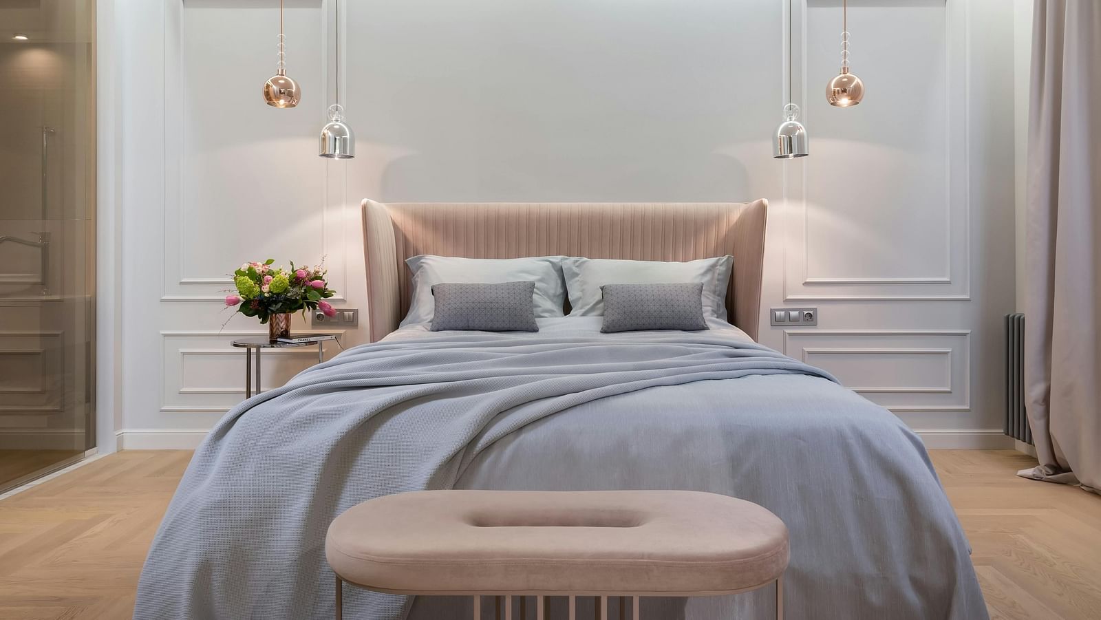 A modern bedroom is shown with soft lighting, a grey duvet, and a tufted bench.
