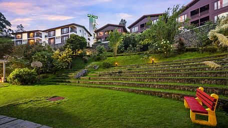 Exterior view of the hotel with lush greenery with the hotel buildings in the background - GReaT Trails Kodaikanal By GRT Hotels