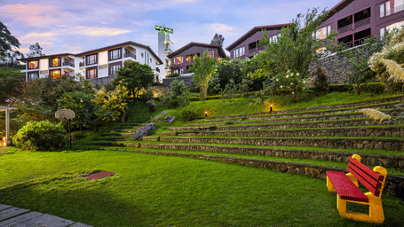 Exterior view of GReaT trails Kodaikanal by GRT Hotels in Kodaikanal at dusk, featuring hillside cottages, landscaped gardens, and illuminated pathways.