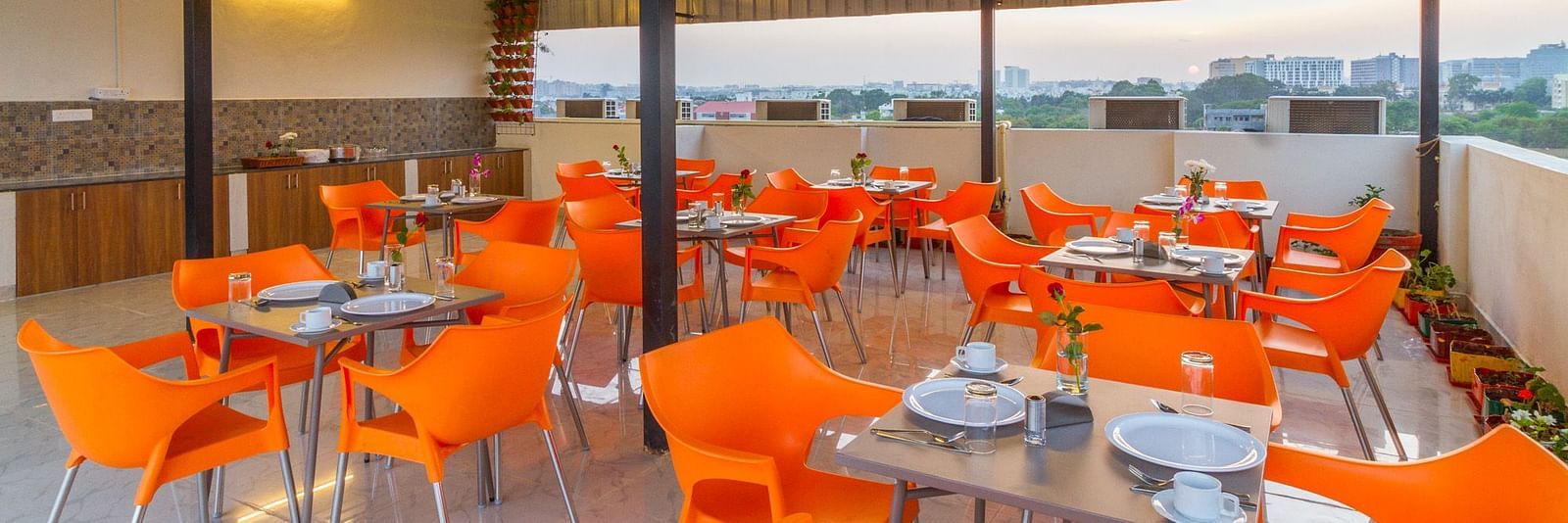 An open-air rooftop dining area with orange chairs and numerous tables at Sanctum Suites Whitefield, Bangalore.