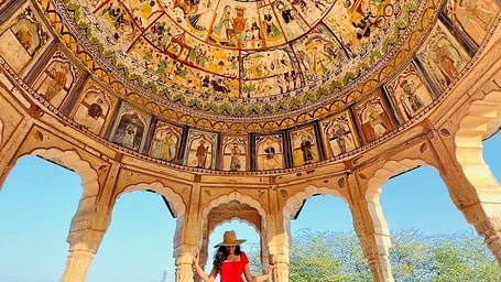 A person stands under a dome with detailed paintings and arched supports - Fort Barli, Ajmer.