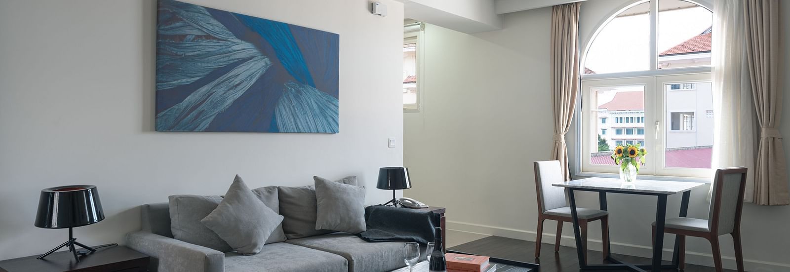 A living room with a grey sofa, a coffee table, and a dining table | One-bedroom Suite | Central Mansions, Phnom Penh