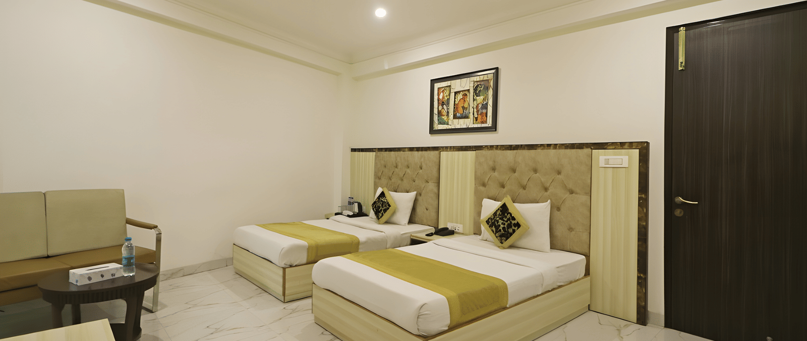 A guest room at Hotel Apple Park Delhi configured with three single beds, white tiled flooring, and a dark wood door