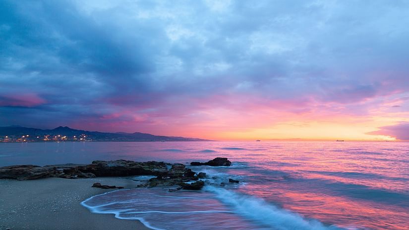 The sky lit up in vibrant colours at the beach, reflecting over the water as the sun sets