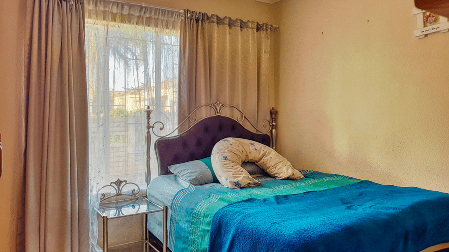 A bedroom featuring a double bed with blue sheets spread neatly over it with beige curtains covering the window behind it.