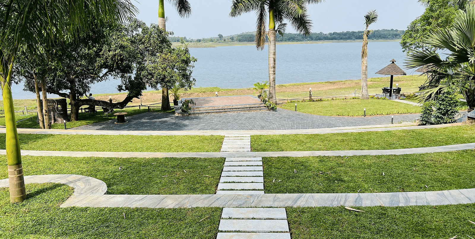 Stone pathway on patches of grass leading to a viewpoint facing the backwaters at Coorg Jungle Camp Backwater Resort in Kushalnagar.